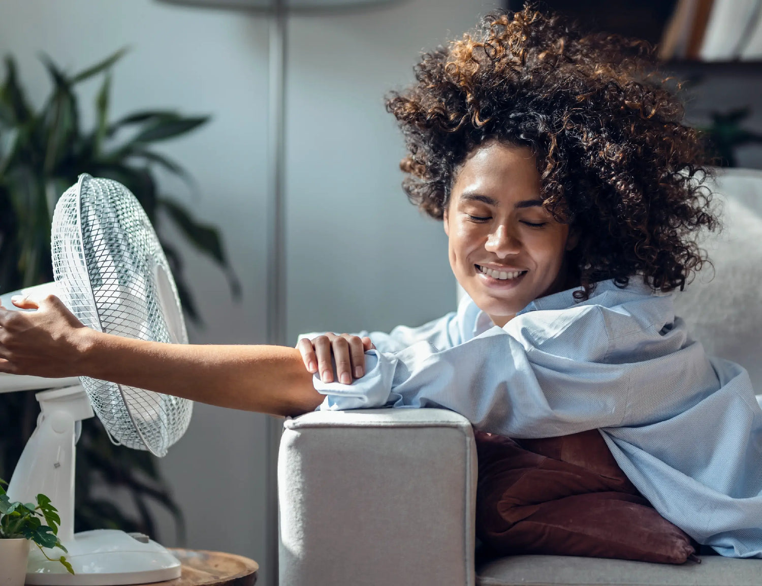 woman enjoying the breeze from a table fan as she sits on a couch